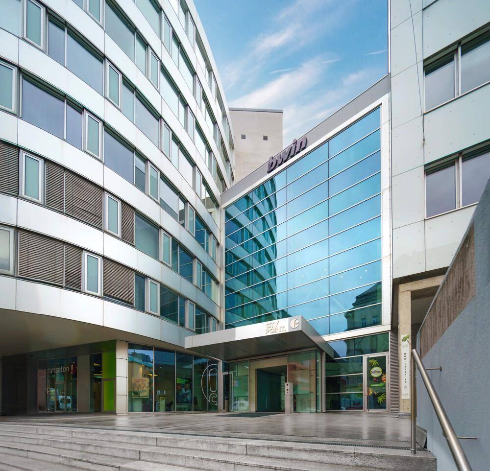 Eingangsbereich eines modernen Bürokomplexes mit großer Glasfassade und Treppenaufgang.