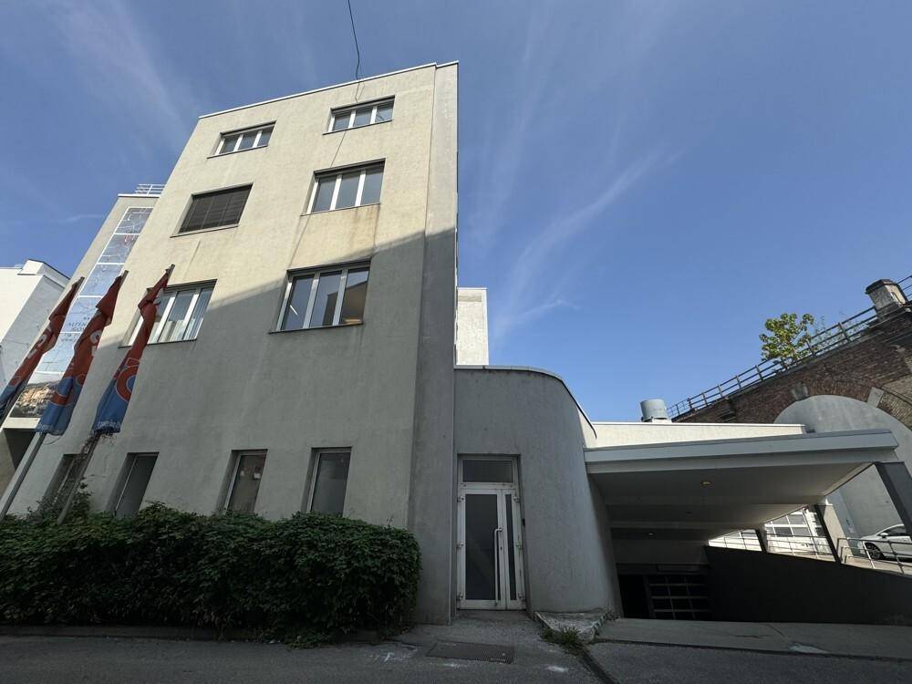 Gebäudefassade mit Haupteingang und Zufahrt zu einer Tiefgarage unter klarem blauem Himmel.