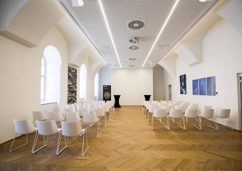 Großer Veranstaltungsraum mit Reihenbestuhlung, hohen Gewölbedecken und modernen Beleuchtungselementen.