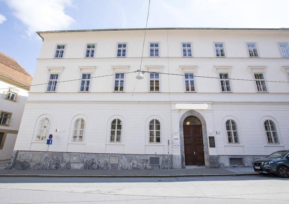 Klassische weiße Fassade eines Mehrfamilienhauses mit vielen Fenstern und einem Holzeingangstor.