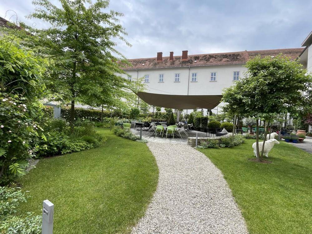 Gepflegter Innenhofgarten mit Kiesweg, Rasenflächen, Bäumen und einem schattigen Sitzbereich für Entspannung.