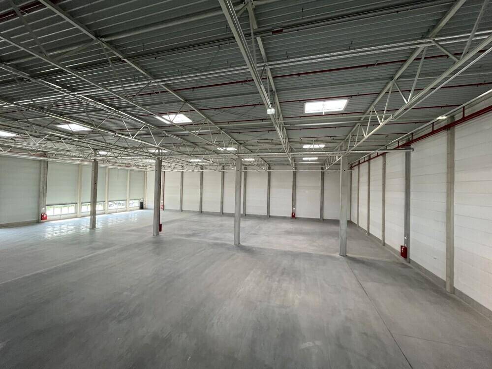 Geräumige, leere Industriehalle mit hohen Decken, Betonboden und sichtbaren Dachkonstruktionen.