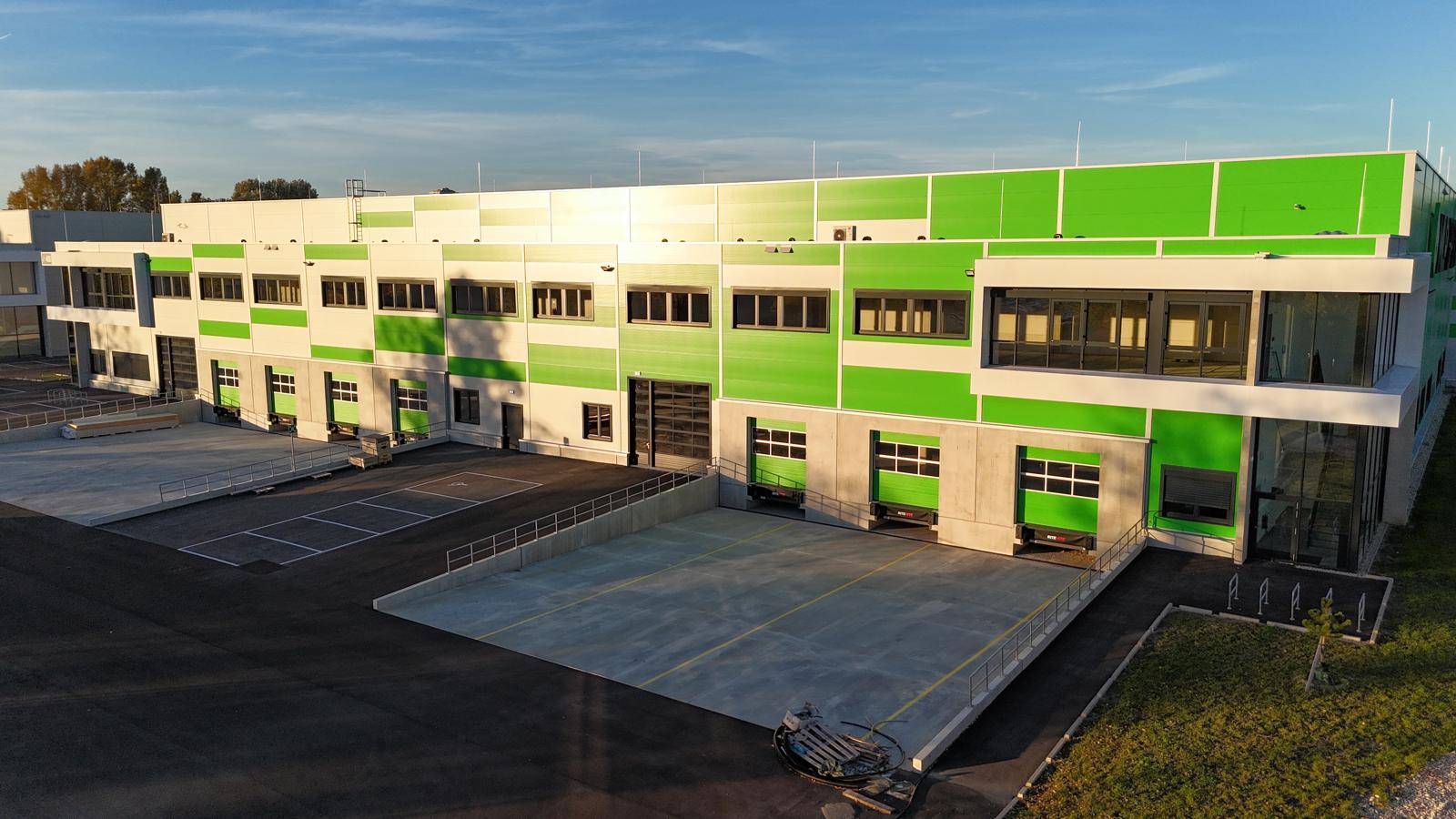 Ansicht einer modernen Gewerbehalle mit mehreren Laderampen und einer auffälligen grün-weißen Fassadengestaltung.