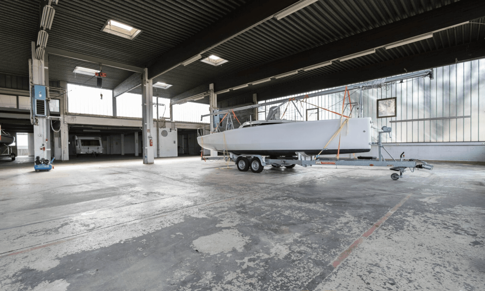 Geräumige Industriehalle mit hoher Decke, Betonboden und einem Boot auf einem Anhänger.