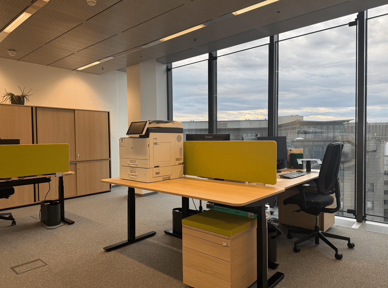 Geräumiges Büro mit mehreren Arbeitsplätzen, großen Fenstern und Blick auf die umliegende Stadtlandschaft.