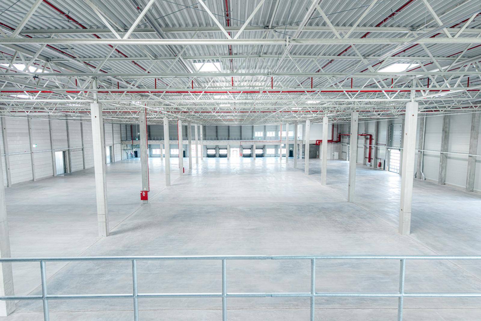 Geräumige, leere Lagerhalle mit hoher Decke, Betonboden und mehreren Laderampen im Hintergrund.