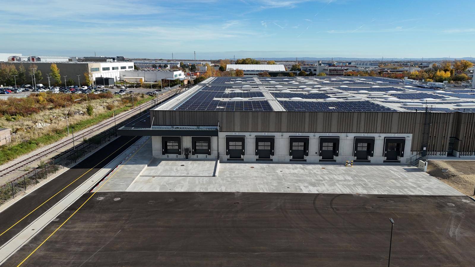 Ansicht der Laderampen eines modernen Industriegebäudes mit großflächiger Solaranlage auf dem Dach.