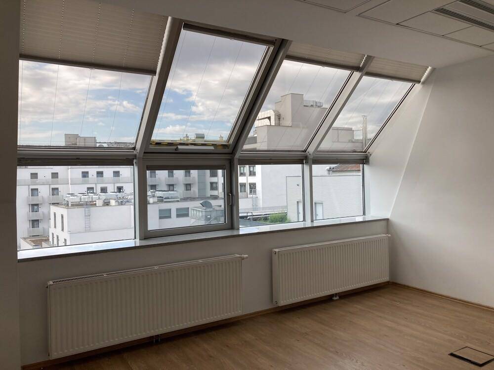Heller Büroraum mit Dachschrägenfenstern, Plissees und Heizkörpern, mit Stadtblick.