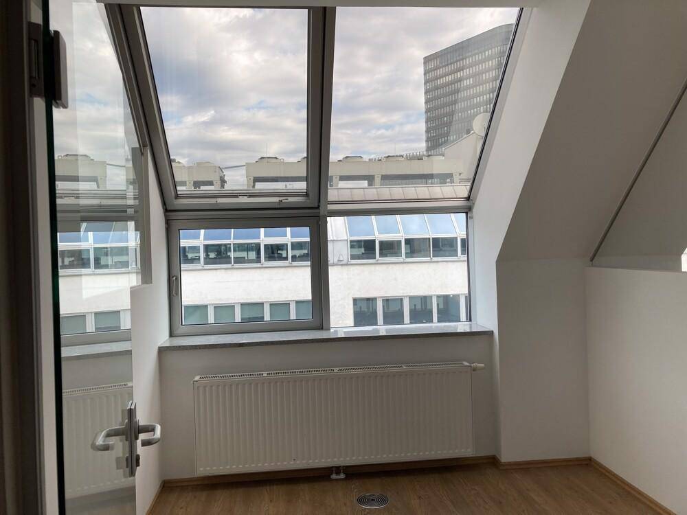 Heller Büroraum mit großen Dachschrägenfenstern und Blick auf moderne Stadtgebäude.