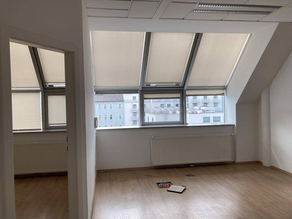 Leerer Büroraum mit Dachschrägenfenstern, Plissees und Heizkörpern, bereit zur Einrichtung.