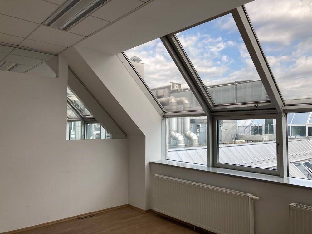 Heller Büroraum mit Dachschrägenfenstern und Blick auf umliegende Gebäude und Dächer.