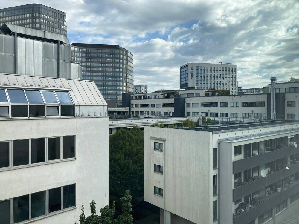 Panoramablick auf moderne Stadtgebäude und grüne Bäume unter bewölktem Himmel.