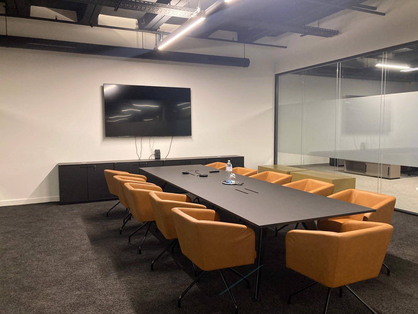 Konferenzraum mit großem Tisch, bequemen Stühlen und Wandfernseher für Präsentationen in modernem Design.