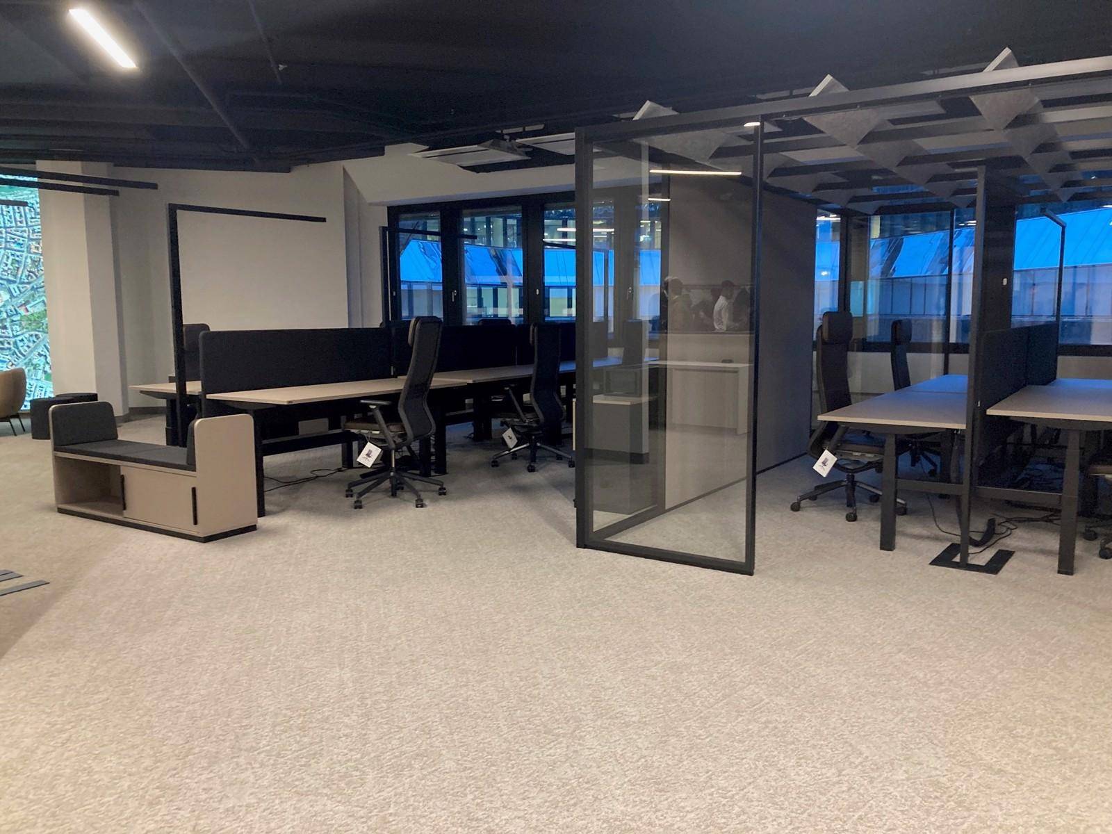 Moderner Großraumbüro-Arbeitsplatz mit ergonomischen Stühlen und Teppichboden, der eine helle Arbeitsumgebung bietet.