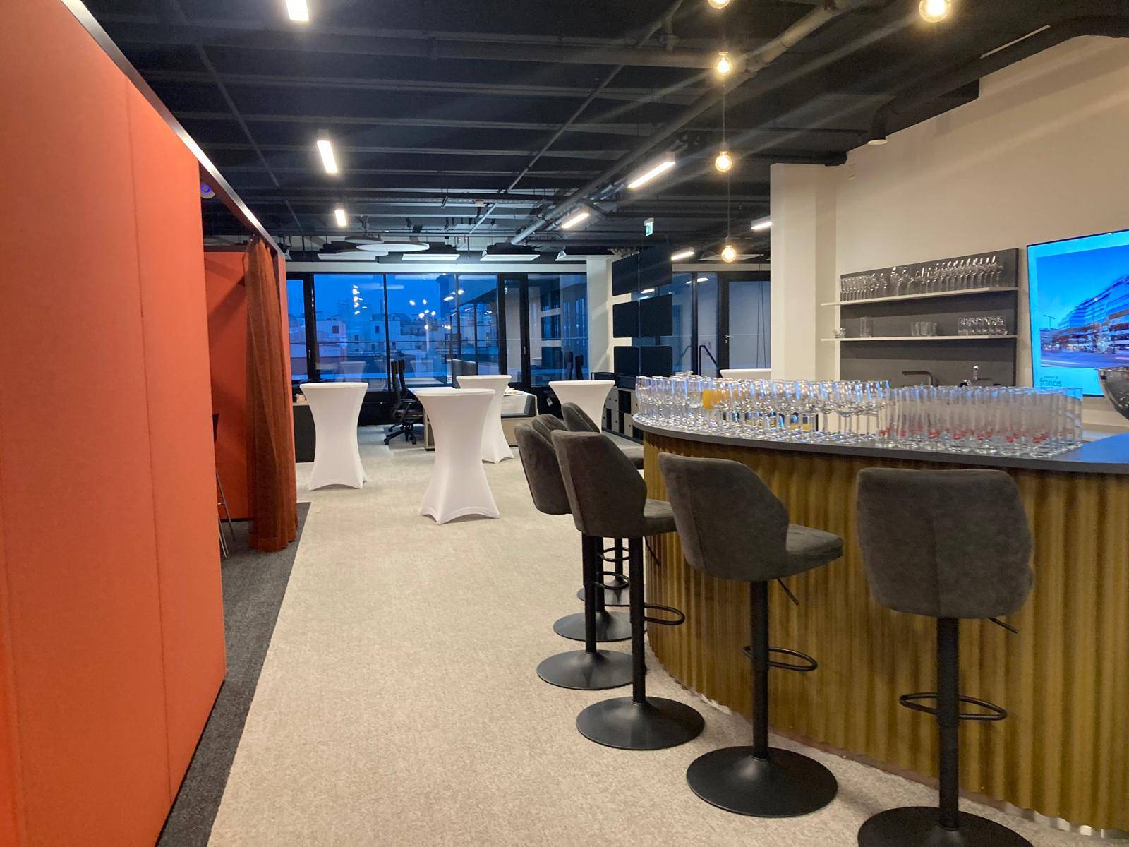 Moderner Bar- und Loungebereich mit hohen Hockern und Blick durch große Fenster, ideal für informelle Treffen.