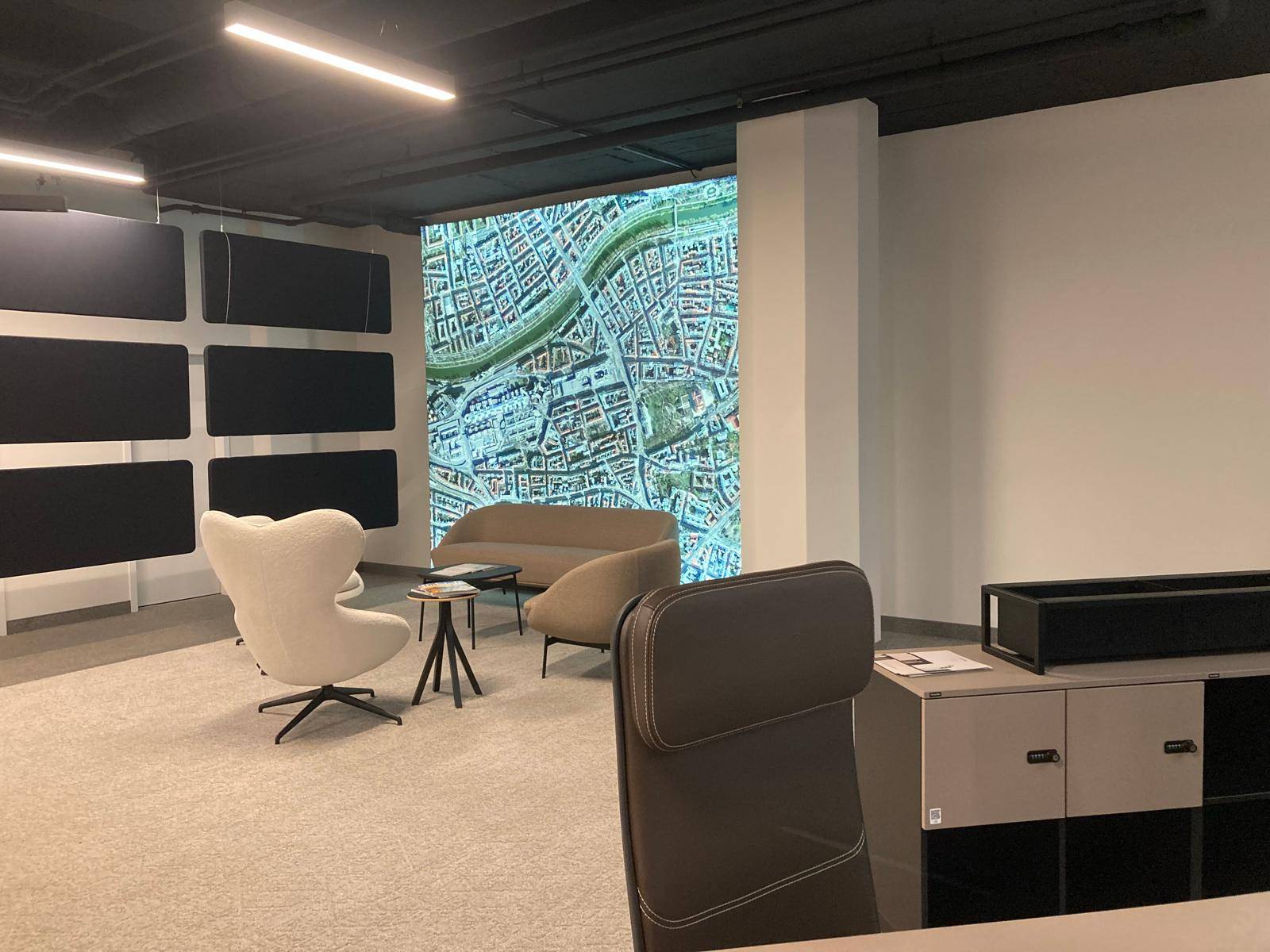 Gemütlicher Loungebereich mit bequemen Sesseln und einer großen Projektion einer Stadtkarte an der Wand.