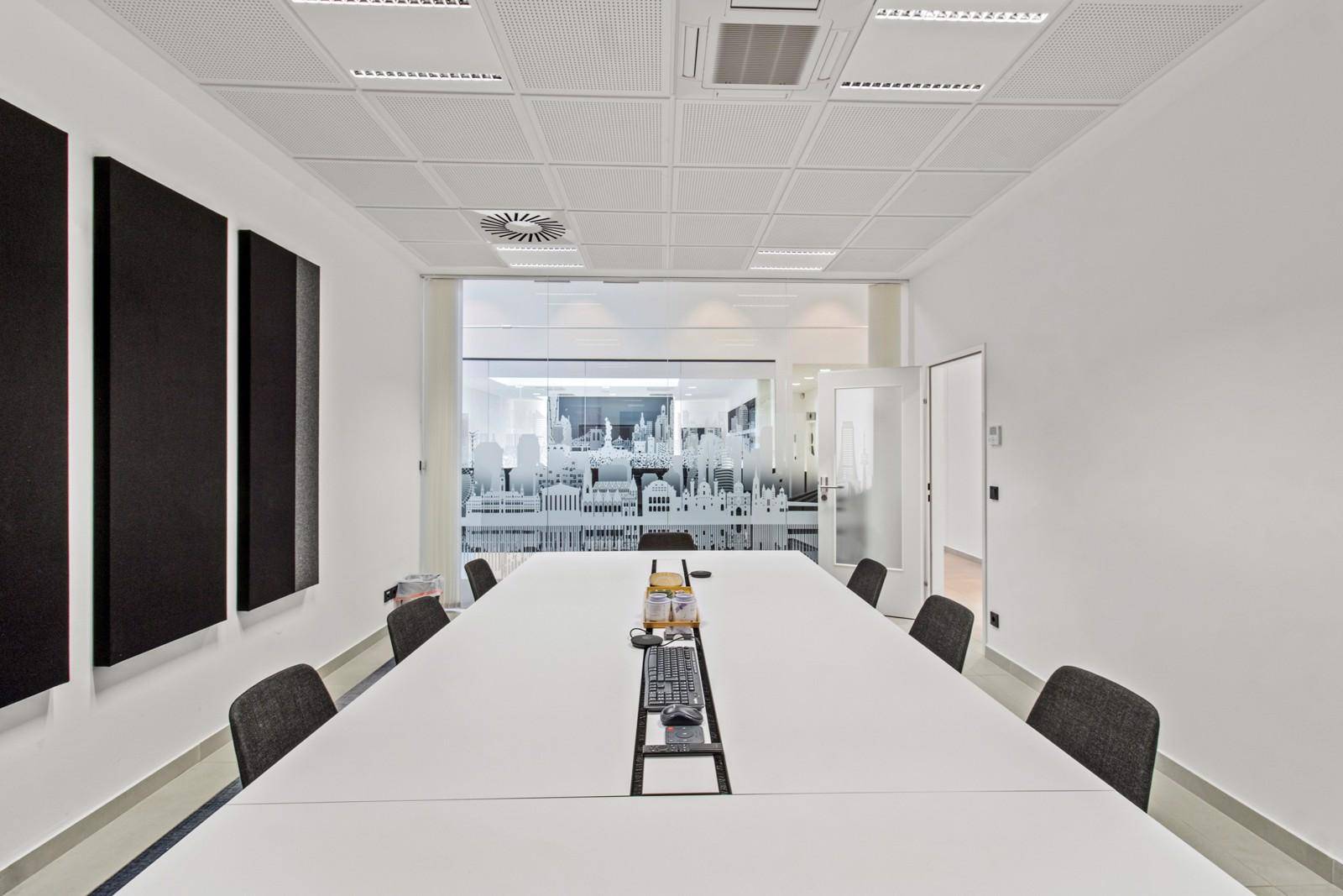 Moderner Konferenzraum mit langem weißen Tisch, Akustikpaneelen und abgehängter Decke.