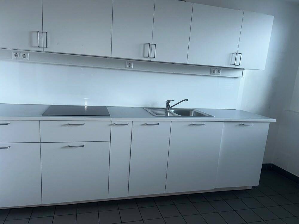 Moderne Küche mit weißen Schränken, Induktionskochfeld und Spüle in einem Bürogebäude.