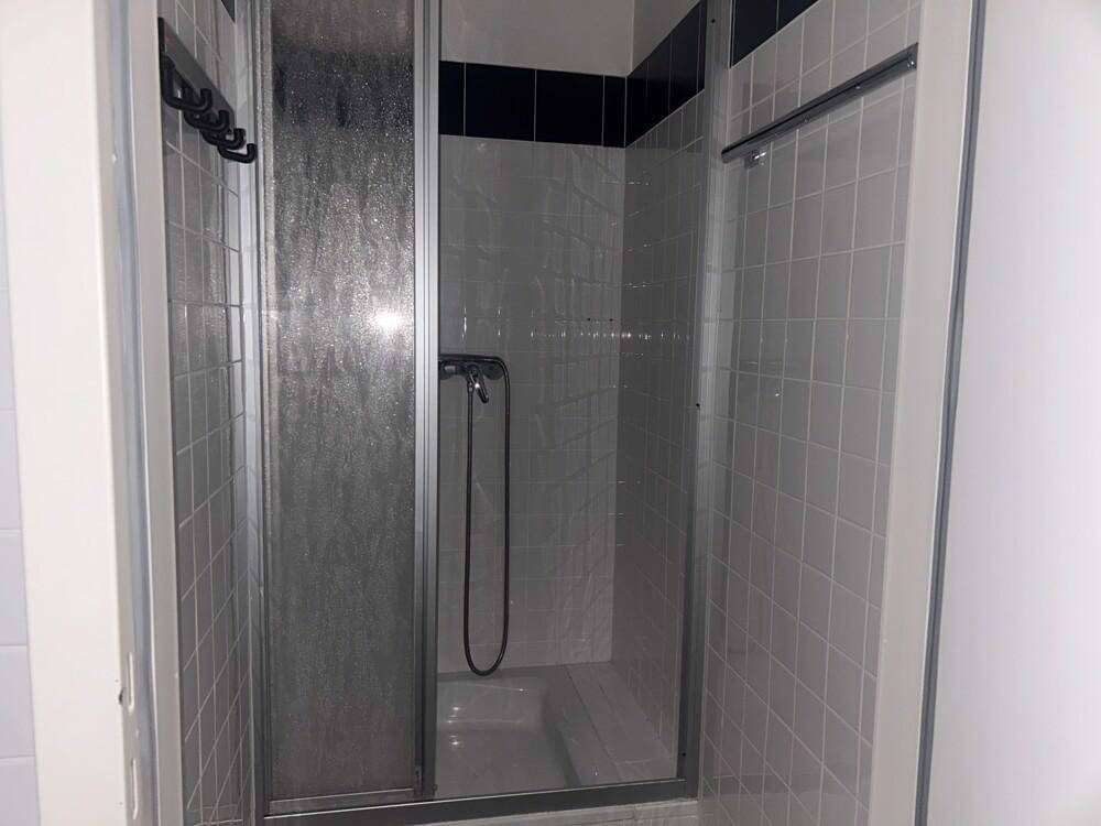 Duschkabine mit Glaswand und weißen Fliesen in einem Badezimmer mit dunklem Akzentstreifen.