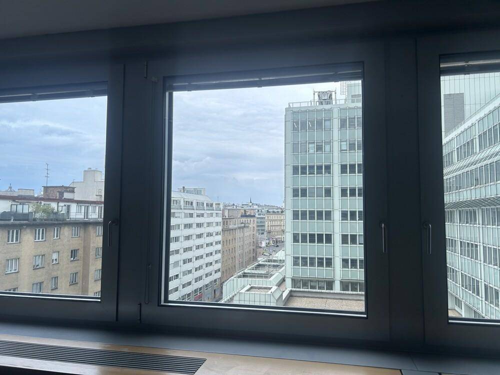 Blick aus einem Fenster auf die umliegende Stadtlandschaft mit verschiedenen Bürogebäuden unter bewölktem Himmel.