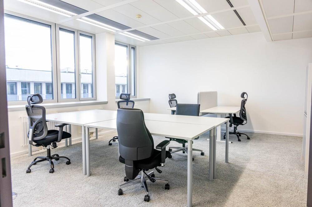 Heller und offener Bürobereich mit mehreren weißen Schreibtischen und ergonomischen Bürostühlen.