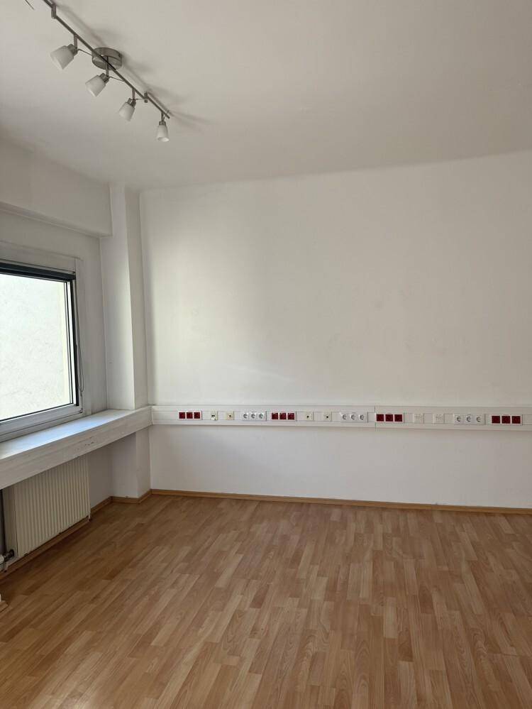 Heller Büroraum mit Laminatboden, weißen Wänden, Fenster und zahlreichen Steckdosenleisten.