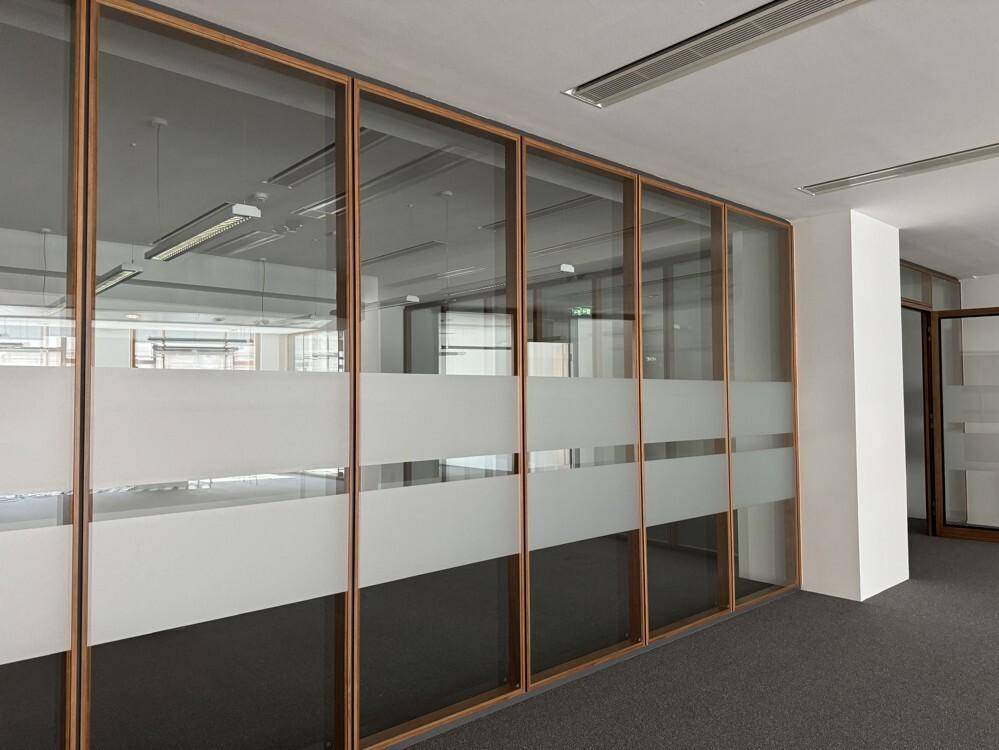Geräumiges Büro mit Glaswänden und Teppichboden, das viel Tageslicht hereinlässt.