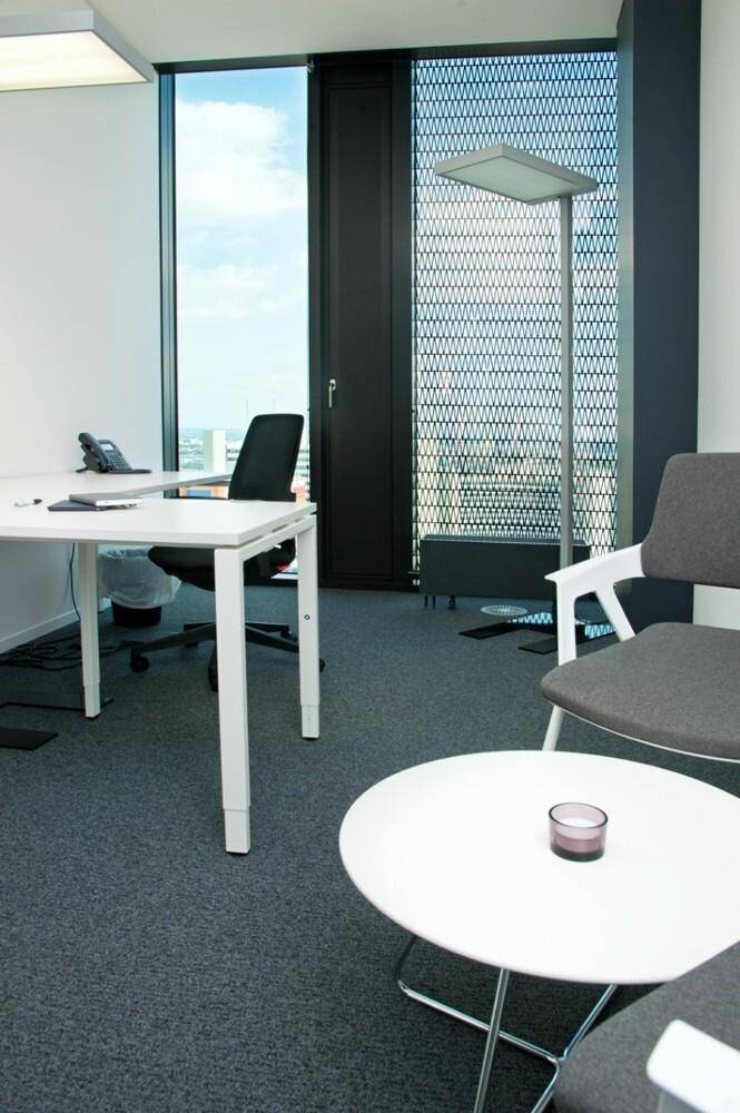 Gemütliche Sitzecke im Büro mit kleinem Tisch und Stühlen, neben einem Fenster mit Muster.