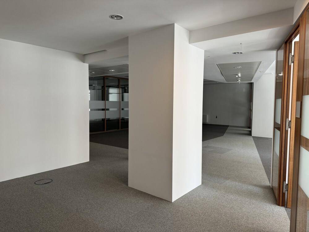 Offener Bürobereich mit Säulen, Teppichboden und Zugang zu weiteren Räumen durch Holztüren.