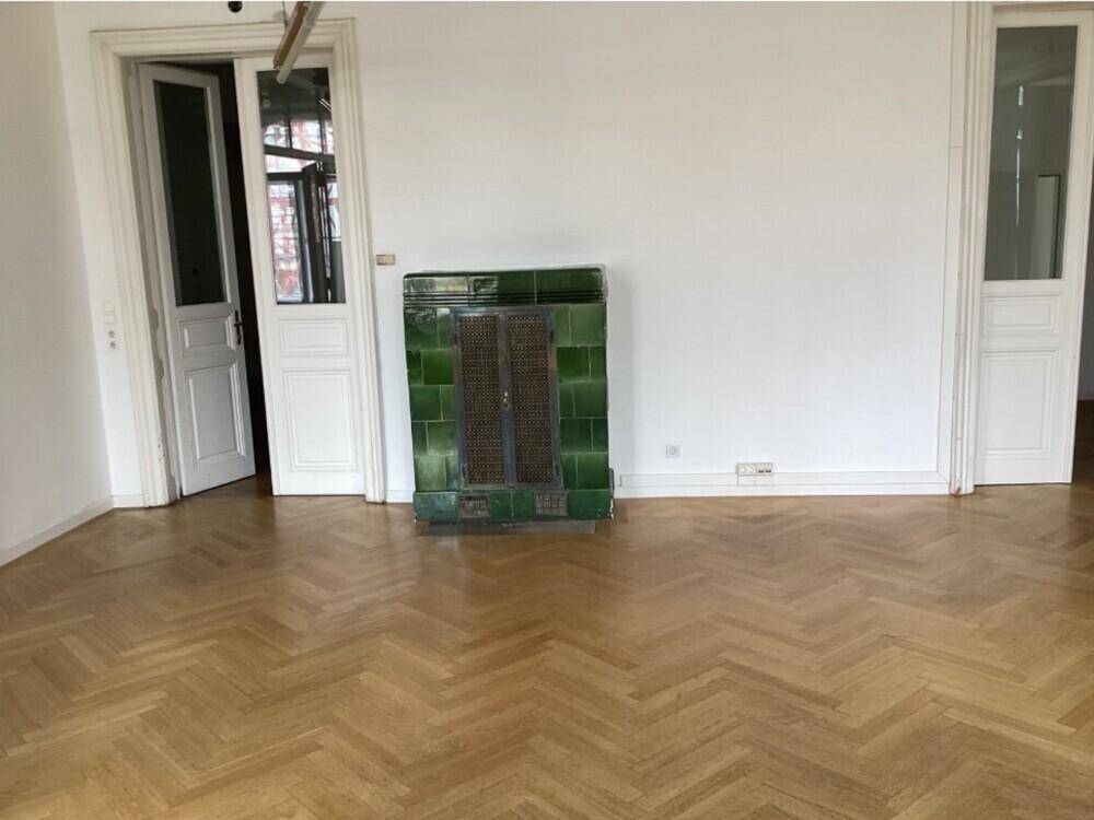 Helles Zimmer mit Fischgrätparkett und einem traditionellen grünen Kachelofen als Blickfang.