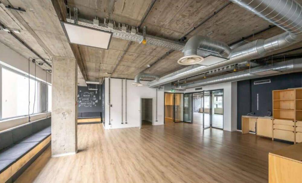 Geräumiges Büro mit Holzboden, Sichtbetondecke und einer Sitzbank am Fenster mit Stadtblick.