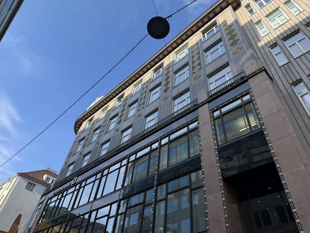 Fassade eines Geschäftsgebäudes mit großen Fenstern und dekorativen Elementen unter blauem Himmel.