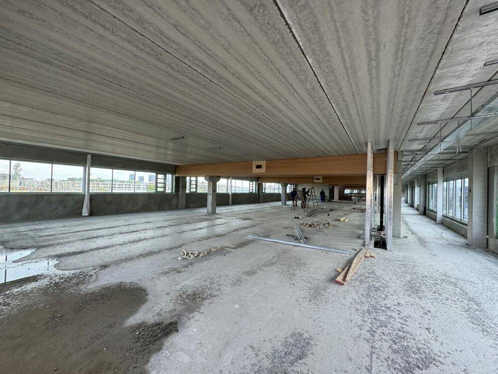 Ein weitläufiger, unfertiger Gewerberaum mit Betonboden, Holzträgern und großen Fensterfronten während der Bauphase.