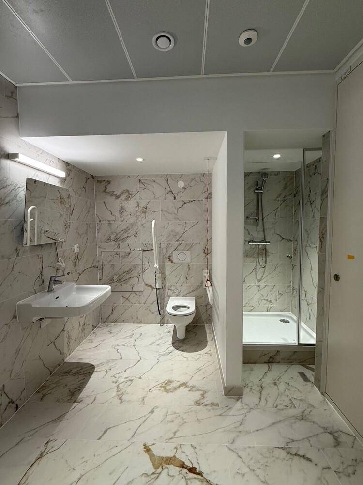 Barrierefreies Badezimmer mit Marmorfliesen, Dusche und Haltegriffen für zusätzliche Sicherheit.