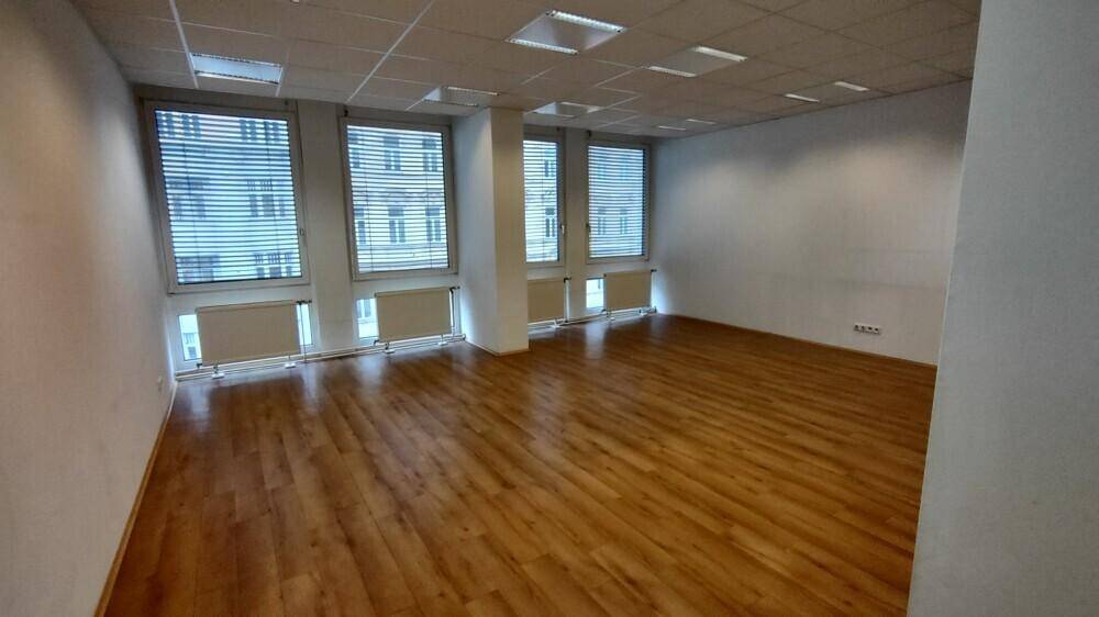 Heller Büroraum mit Holzboden, Rasterdecke und mehreren Fenstern mit Jalousien für Privatsphäre.