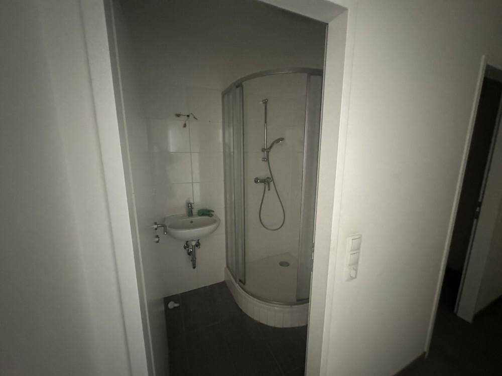 Kleines Badezimmer mit Eckdusche, wandmontiertem Waschbecken und dunklen Fliesen auf dem Boden.