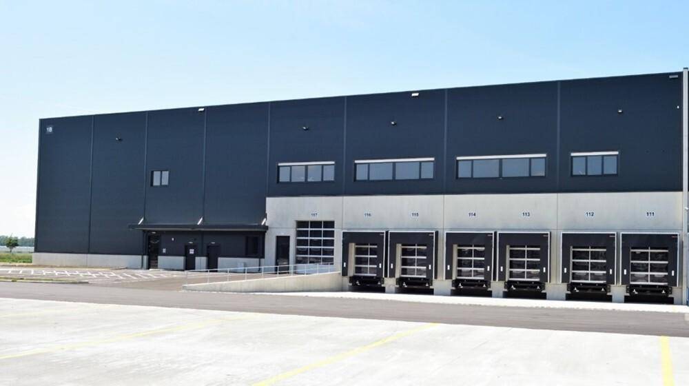 Ansicht der modernen Logistikhalle mit mehreren Laderampen und Zufahrtsbereich bei Tageslicht.