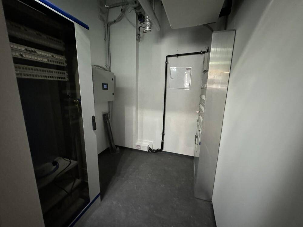 Technikraum mit Serverschrank, Kabeln und Wandinstallationen, funktional und schlicht gestaltet.