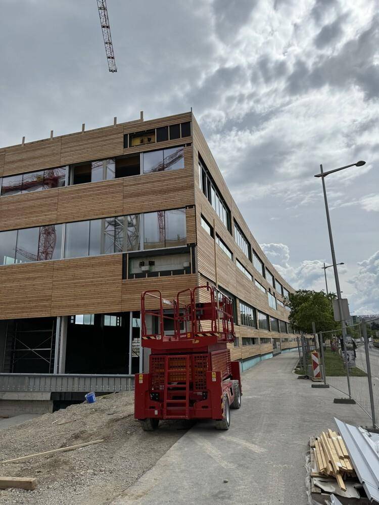 Ein im Bau befindliches modernes Gebäude mit Holzfassade und großen Fensteröffnungen unter bewölktem Himmel.