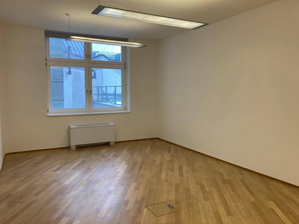 Geräumiges Büro mit Holzboden und einem großen Fenster, das viel Tageslicht hereinlässt.