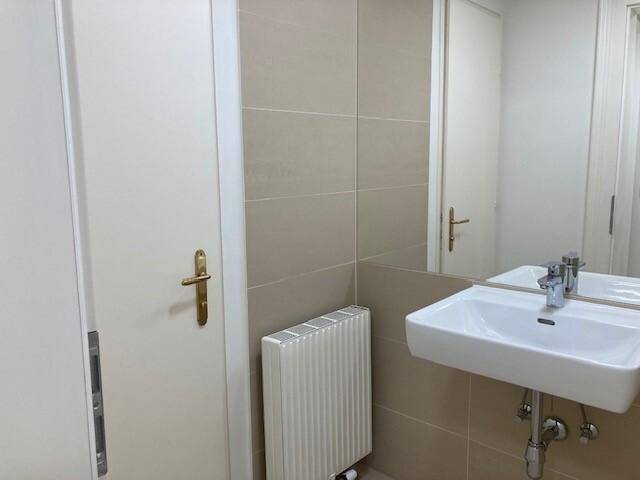 Modernes Badezimmer mit beigefarbenen Fliesen, einem wandmontierten Waschbecken und einem Heizkörper.