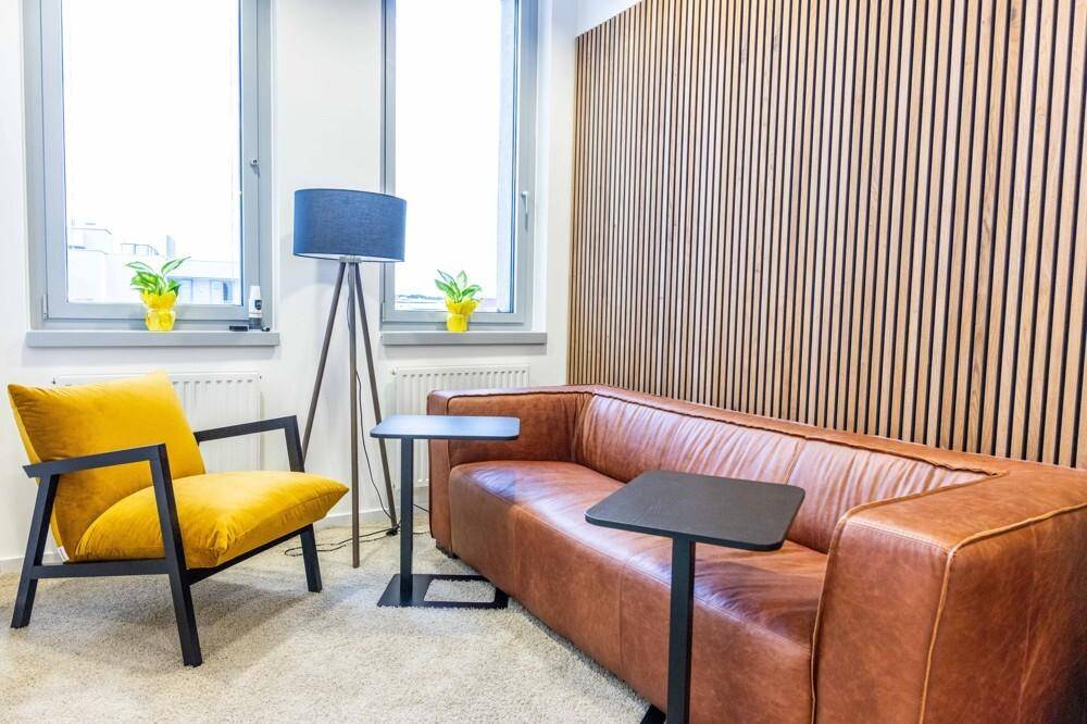 Gemütlicher Loungebereich mit Ledersofa, gelbem Sessel, Stehlampe und einer Holzwandverkleidung.