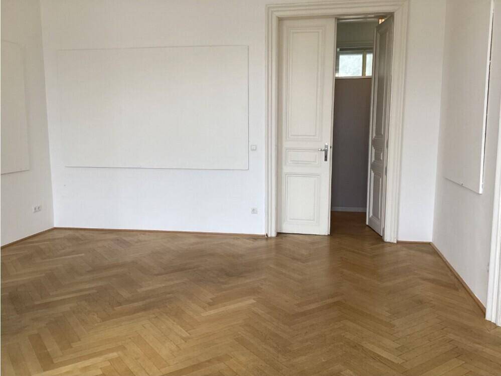 Helles Zimmer mit Fischgrätparkett, weißen Wänden und einer Doppeltür.