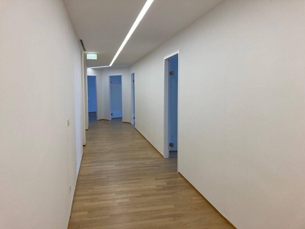 Langer, heller Flur mit Holzboden und mehreren Türen, die zu Büroräumen führen.