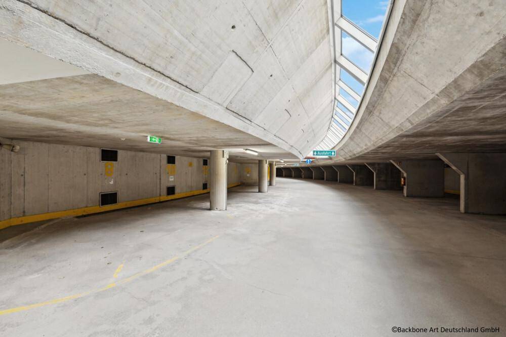 Geräumige Tiefgarage mit Betonwänden und -decken, beleuchtet durch Oberlichter und künstliches Licht.