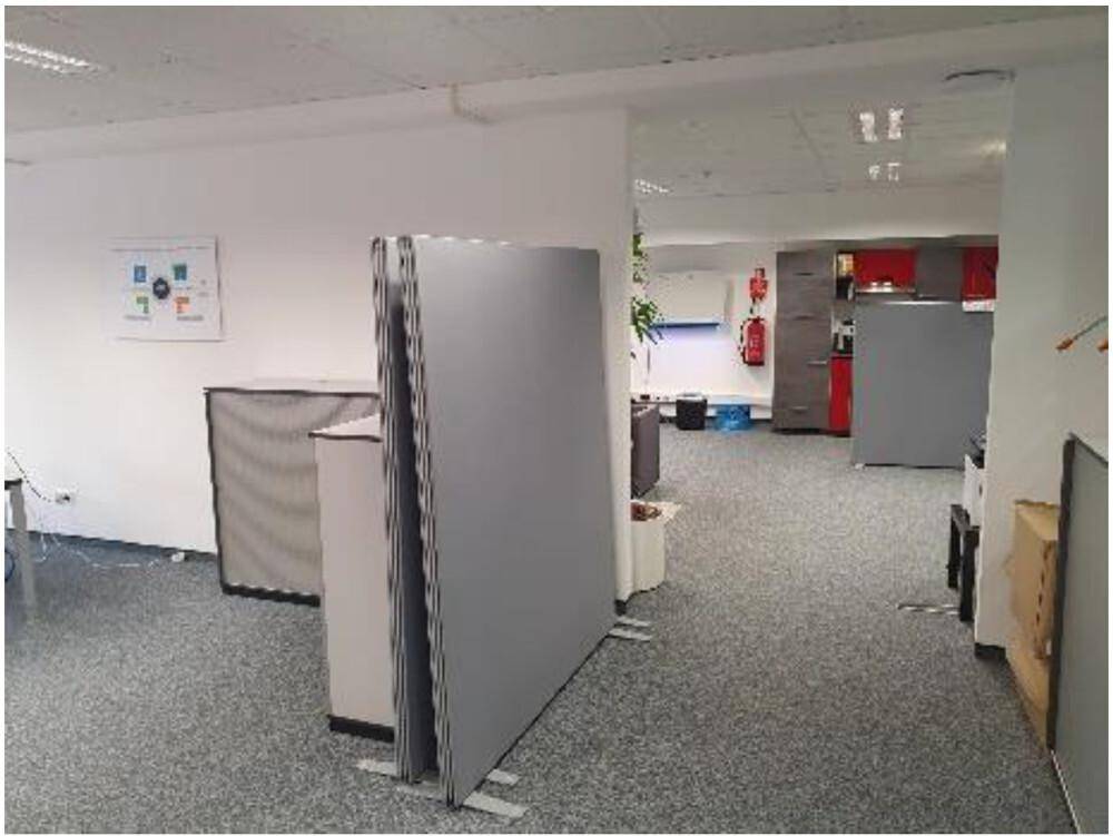 Offener Bürobereich mit flexiblen Trennwänden und Blick auf eine weitere Zone mit roten Schränken.