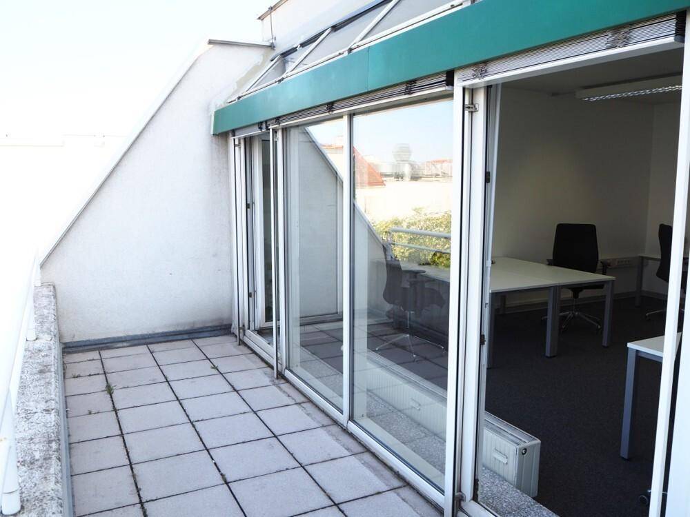 Geräumige Dachterrasse mit Fliesenboden und großen Glasschiebetüren, die zu einem Büroraum führen.