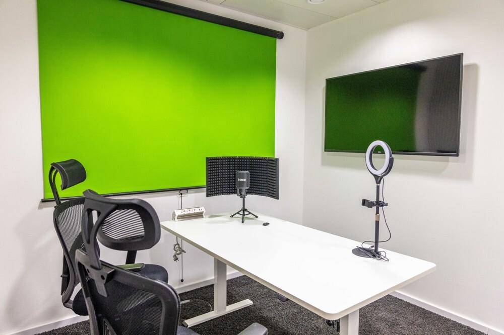 Kleiner Aufnahmeraum mit Greenscreen, Mikrofon und Ringlicht, ideal für Podcasts oder Videoproduktionen.