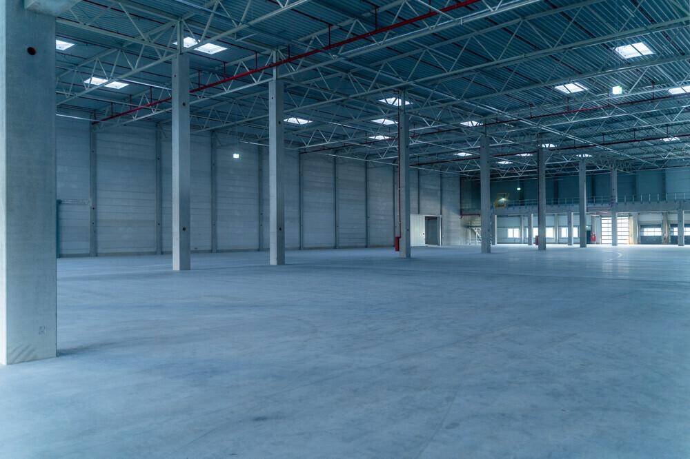 Weitläufige, unmöblierte Lagerhalle mit Betonboden und sichtbaren Stützpfeilern unter der hohen Decke.