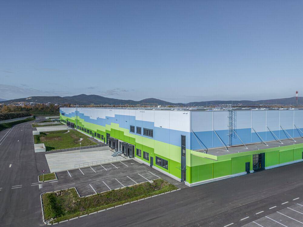 Seitenansicht des modernen Logistikgebäudes mit Laderampen und farbiger Fassadengestaltung unter blauem Himmel.